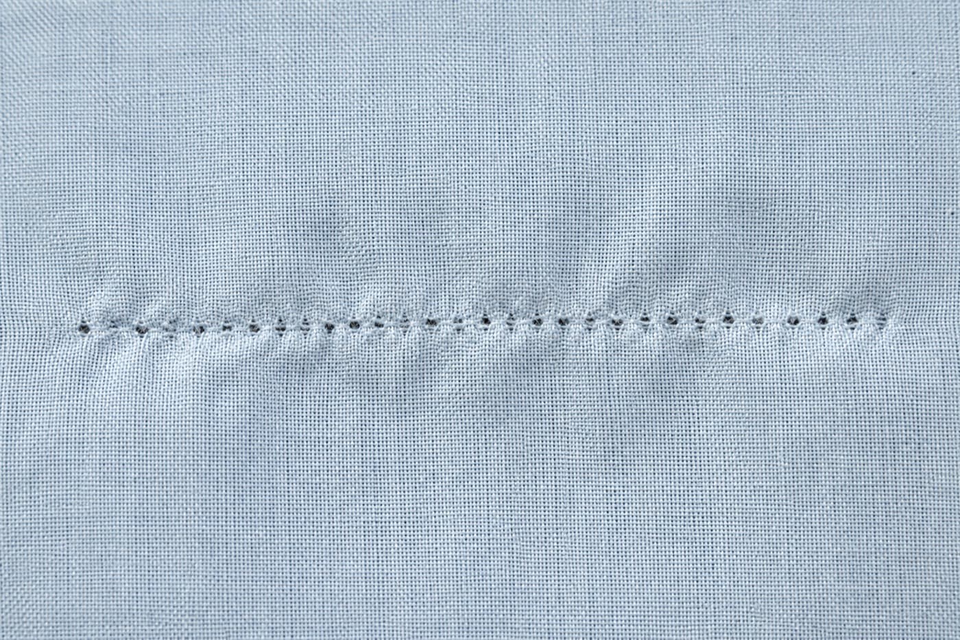 Macro photograph of the empty needle holes left in cotton after a seam has been unpicked
