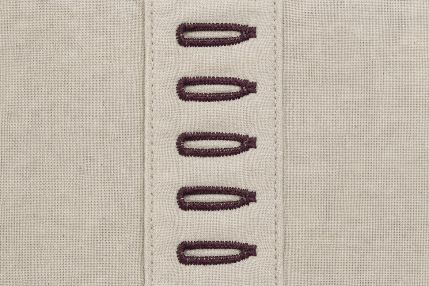 Macro photograph of a vertical row of five finished machine-worked buttonholes